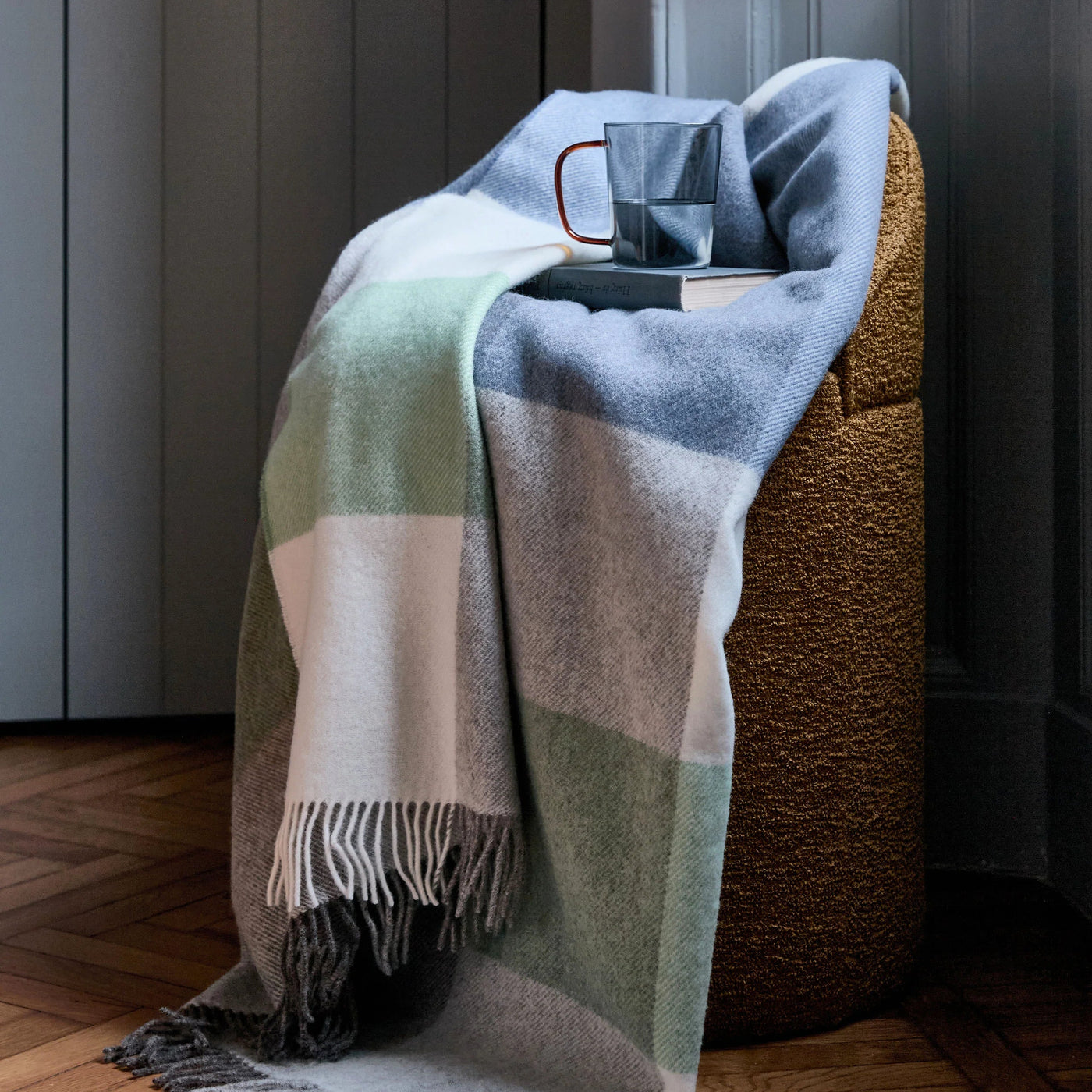 Lanerossi Uruguay GOTS Check throw in sage, blue, and blush draped over a textured ottoman.