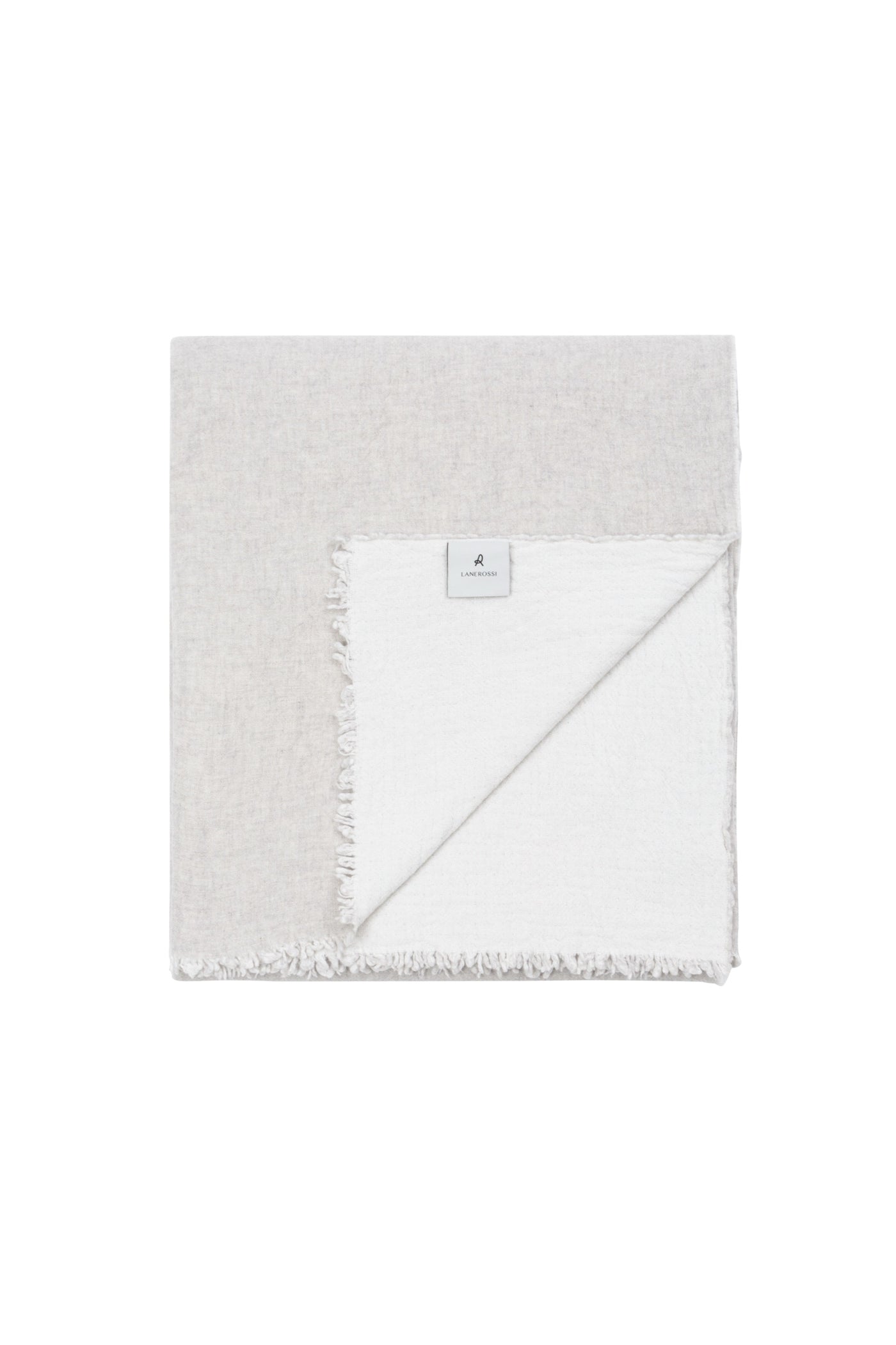 Folded blanket corner turned back showing oatmeal and white reversible linen with fringe trim.