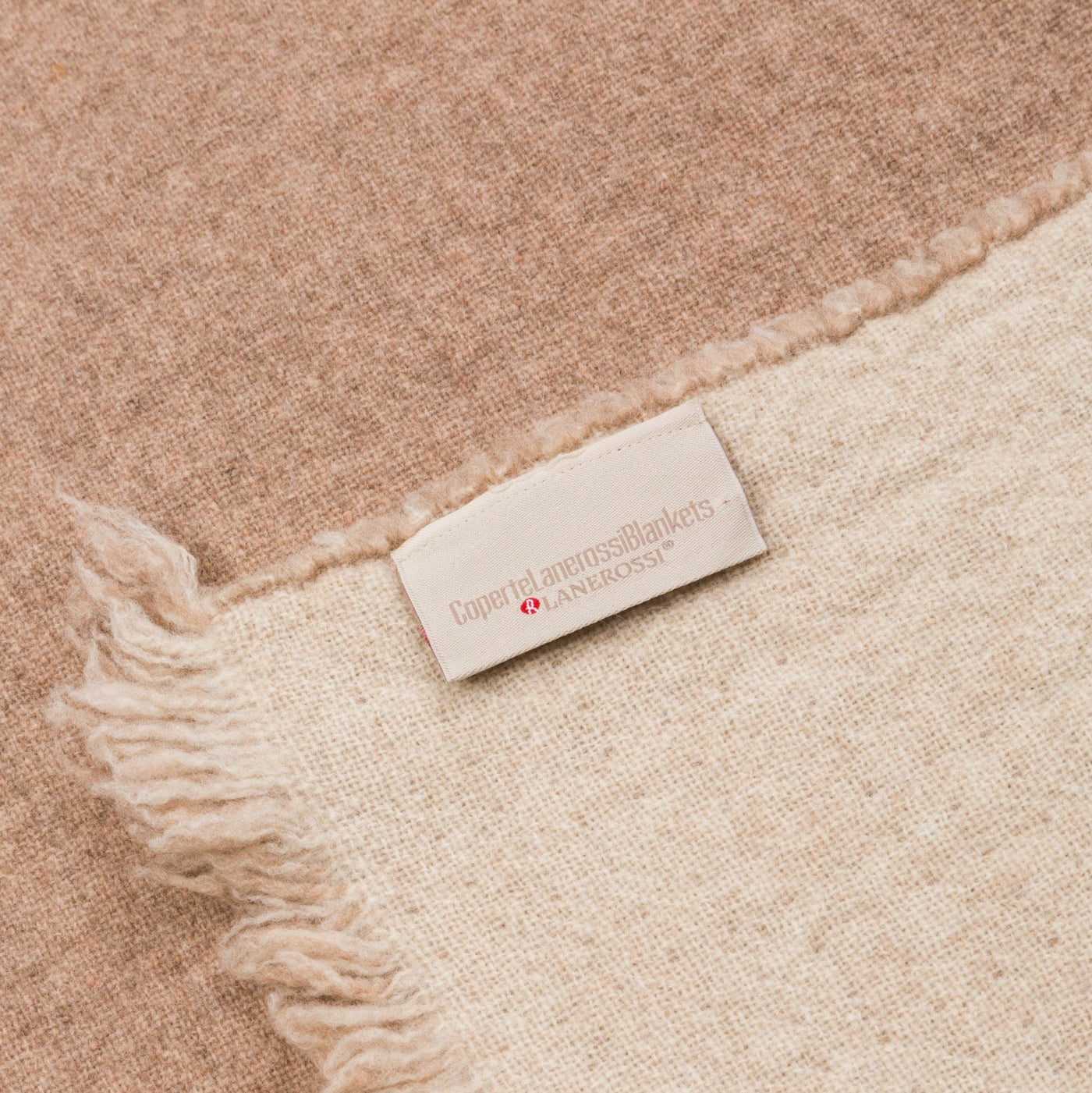 Close-up of Lanerossi woven label on folded camel and ivory wool blanket with fringe edge.
