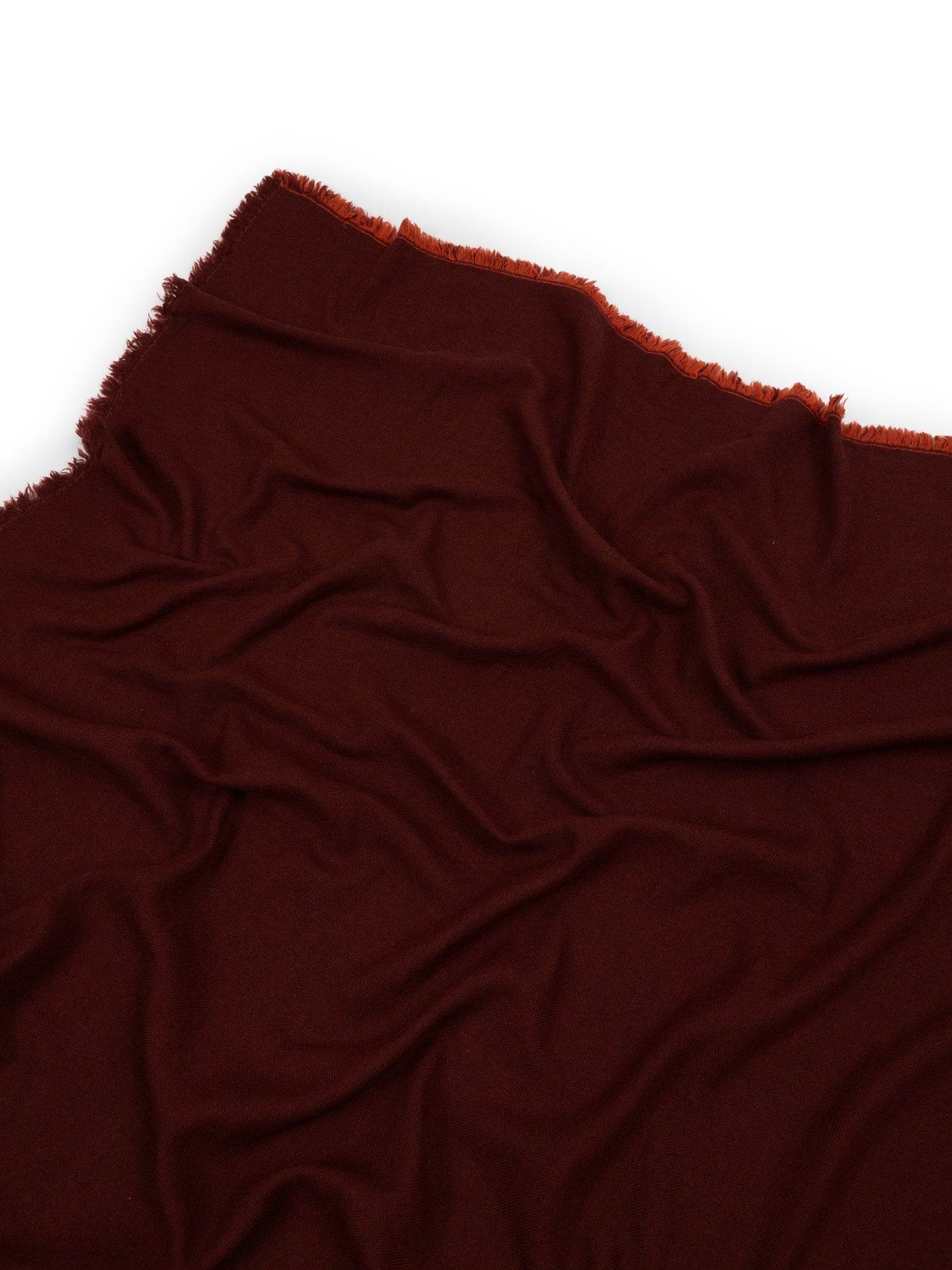 Close-up of draped burgundy throw with rust fringe trim along top edge.