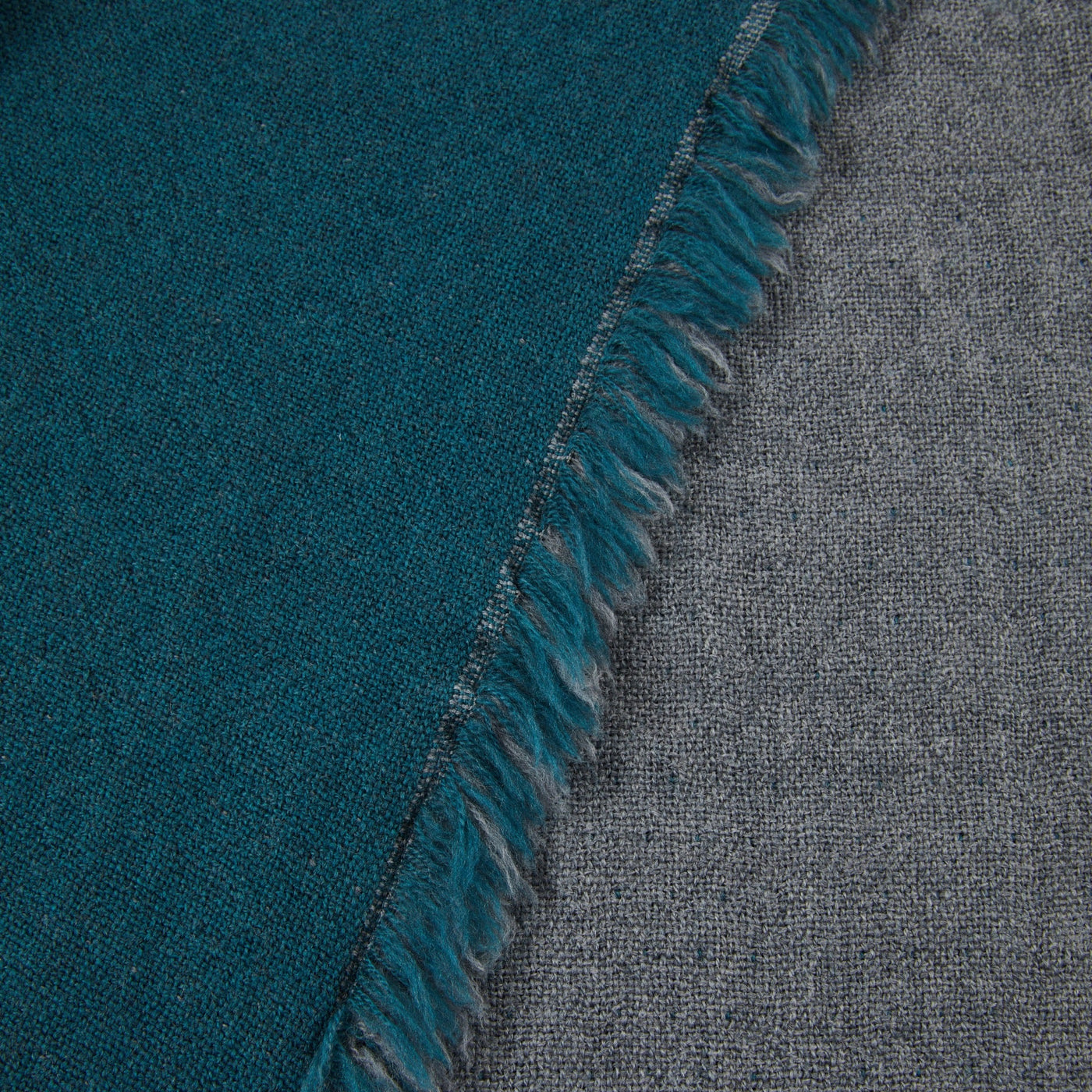 Close-up of teal and grey reversible wool throw showing fringed edge detail.