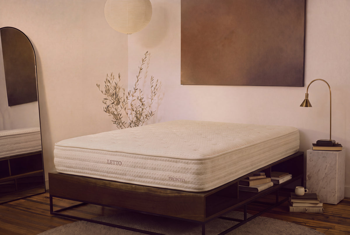 A white quilted mattress on a dark wooden platform bed frame in a styled bedroom setting with a floor mirror, a brass lamp, and a marble side table.