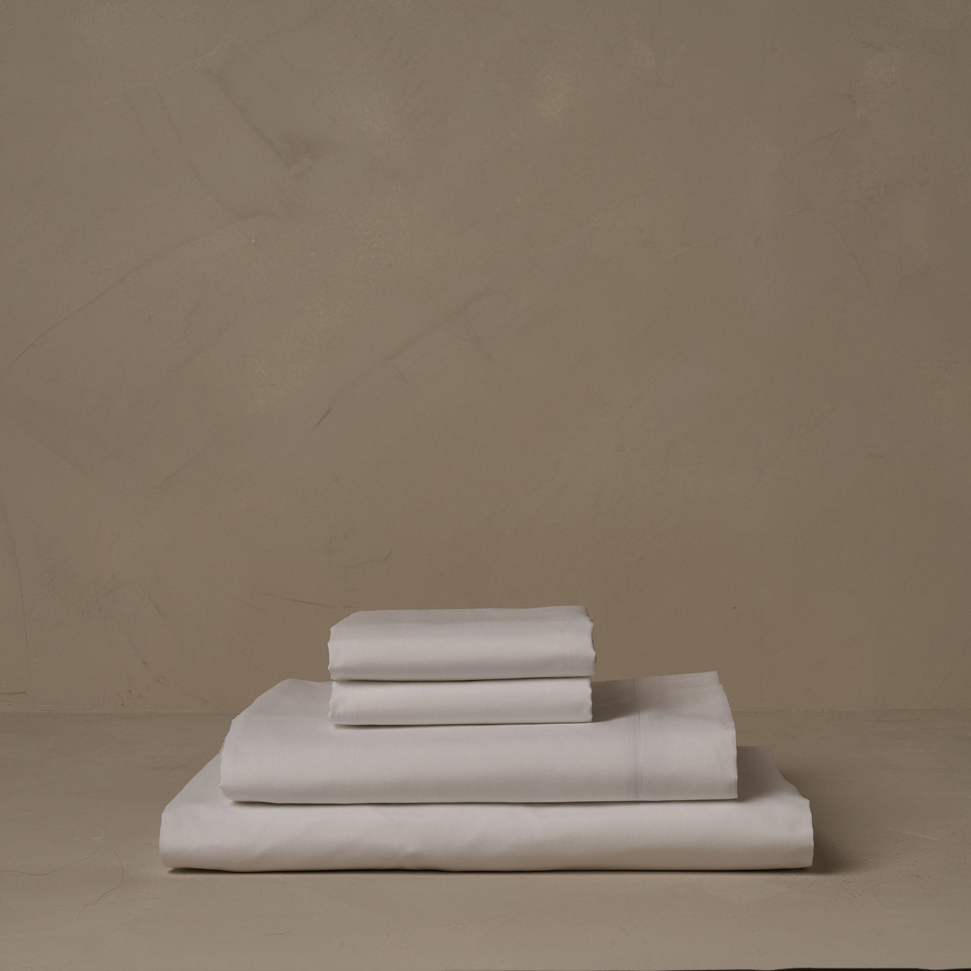 A stack of crisp and cool white Americano Cotton Percale sheets.  The sheets are made in Italy of American cotton. The set includes a fitted sheet, a flat sheet, and a pair of pillowcases.