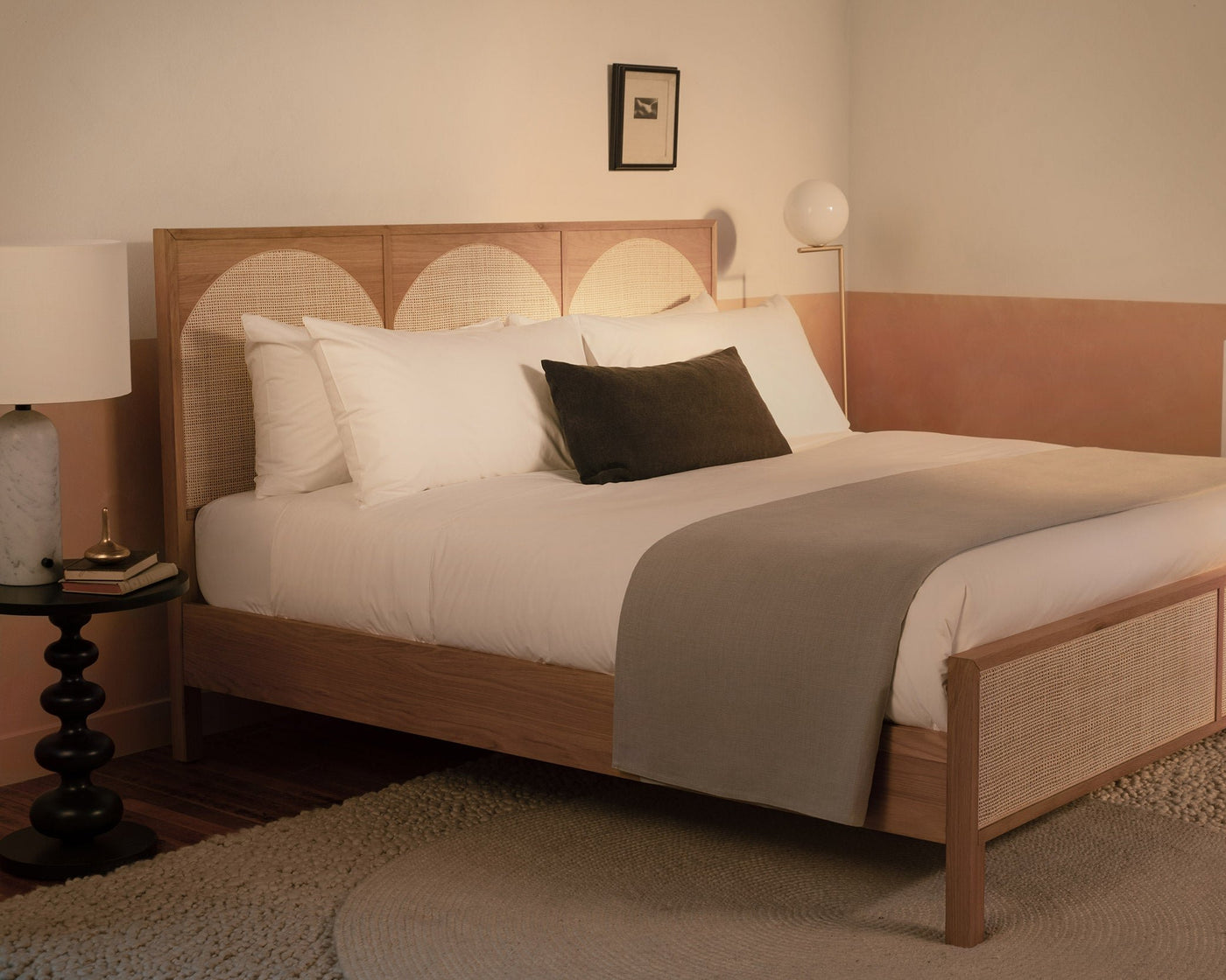 A bedroom with a contemporary wood and rattan bed made with LETTO Americano Cotton Percale sheets, a gray blanket folded at the foot of the bed, and a charcoal velvet throw pillow.