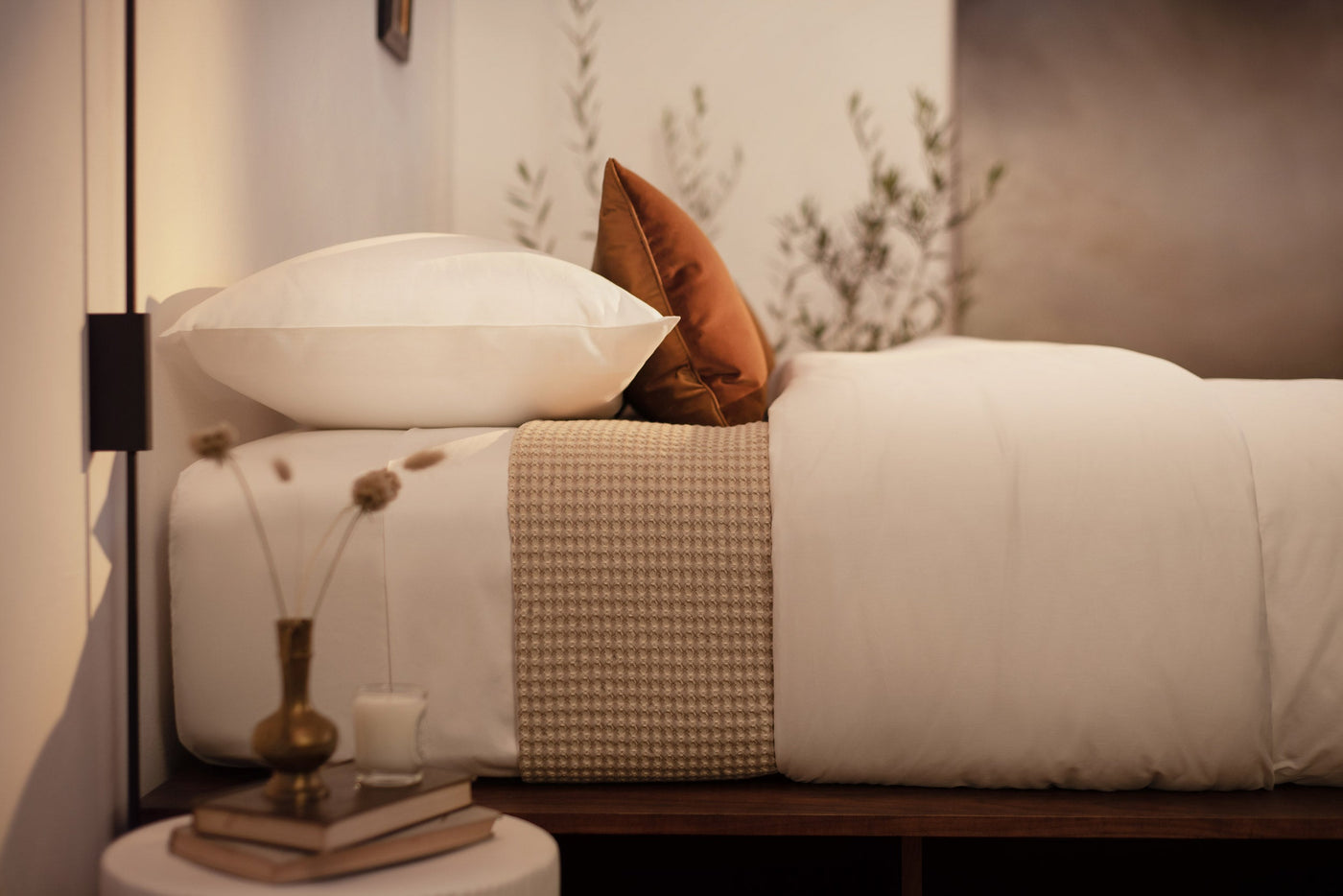 A close up picture of a bed made with LETTO White Classic Cotton Sateen sheets and duvet cover, with a Nido waffleweave blanket in beige and an orange velvet throw pillow.