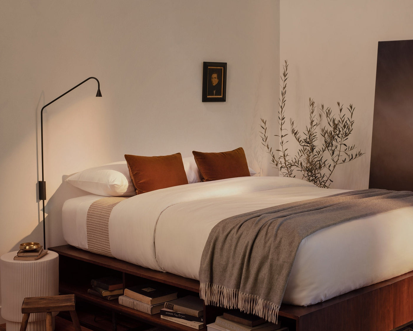 A bedroom with a contemporary platform bed made with LETTO White Classic Cotton Sateen sheets and duvet cover, with a Nido waffleweave blanket in beige,  and a gray Coccola cashmere throw blanket at the foot of the bed.