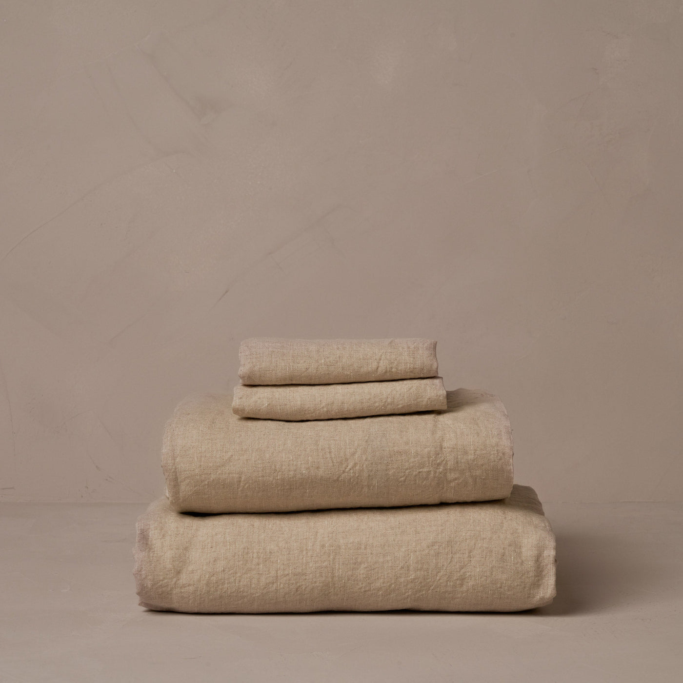 A stack of relaxed and breathable natural colored Classic Linen sheets. Belgian flax, made in Italy. The set includes a fitted sheet, a flat sheet, and a pair of pillowcases.