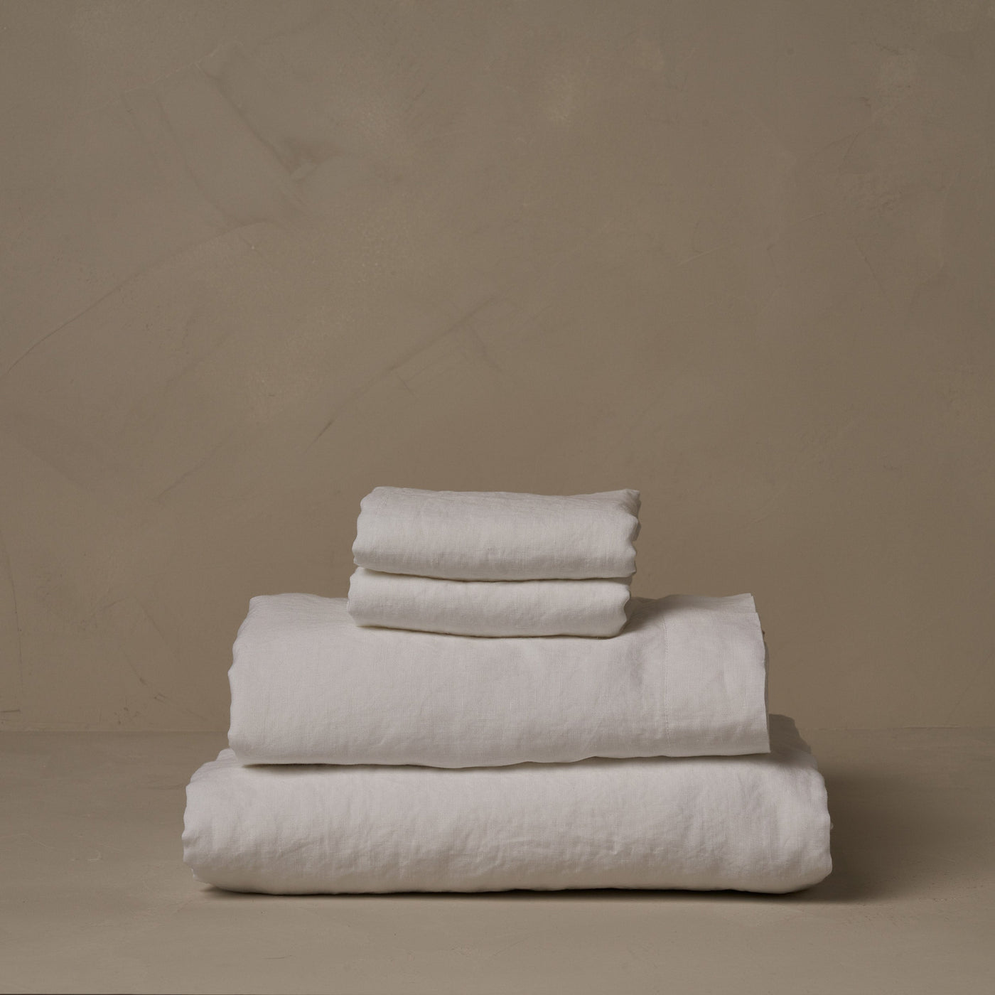 A stack of relaxed and breathable white Classic Linen sheets. Belgian flax, made in Italy. The set includes a fitted sheet, a flat sheet, and a pair of pillowcases.