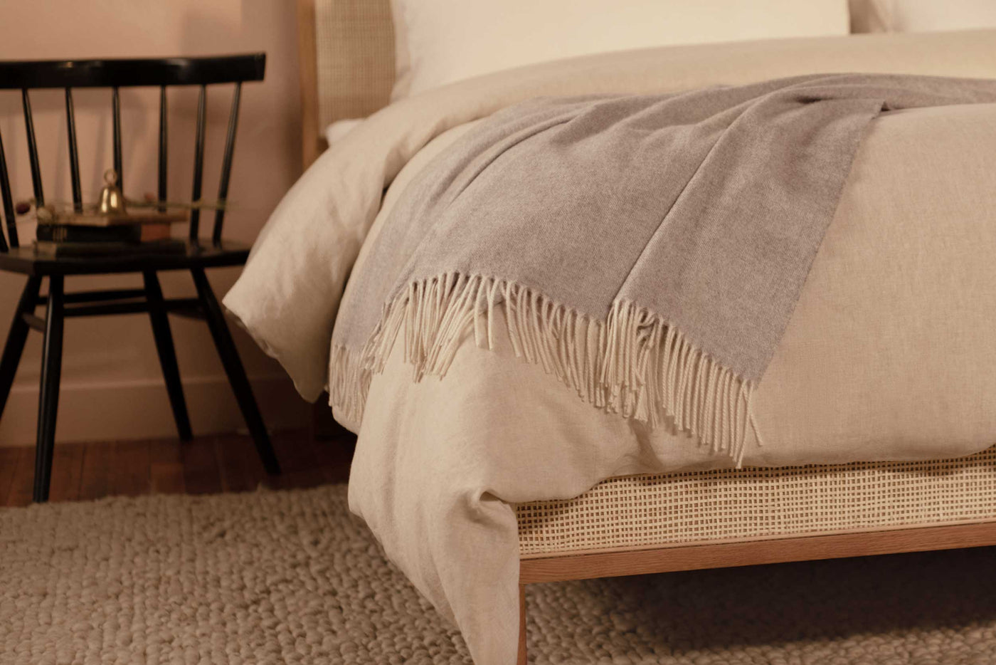 The LETTO Coccola 100% cashmere woven throw blanket in light gray draped at the foot of a bed.