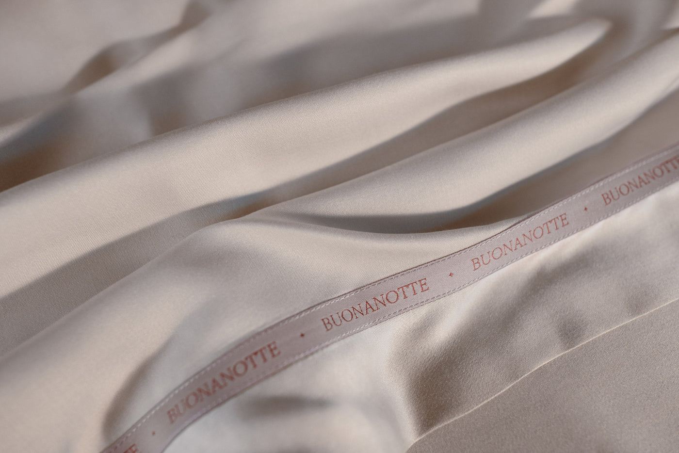 A close up image of the Buonanotte ribbon on the bottom edge of smooth and silky LETTO Woodland Silk beechwood modal flat sheet in color white.