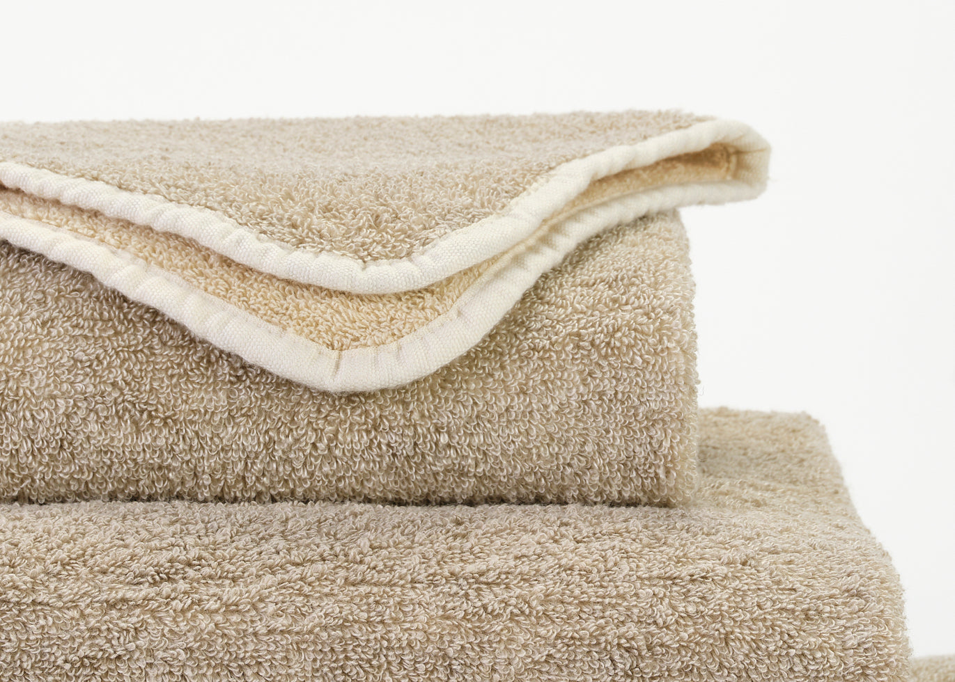 Abyss Habidecor Lino wash cloth in sand and ivory terry cotton, stacked folded towels.