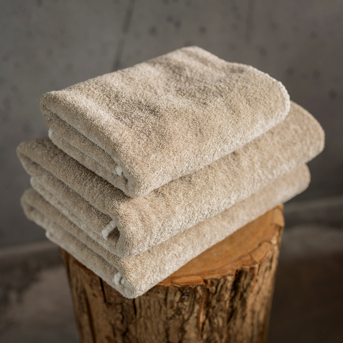Abyss Habidecor Lino euro bath sheet in natural linen, folded stack on wood stump.