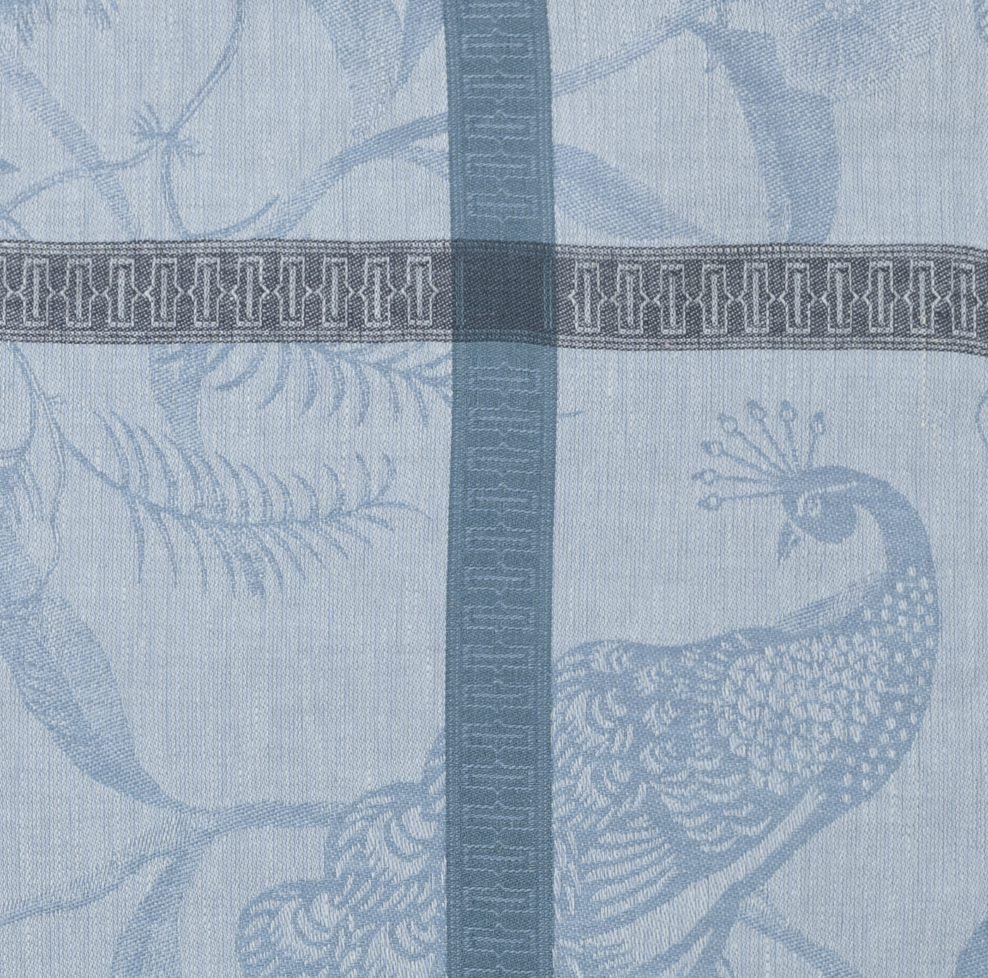 Close-up of slate blue jacquard weave showing peacock and foliage motif with geometric border stripe.