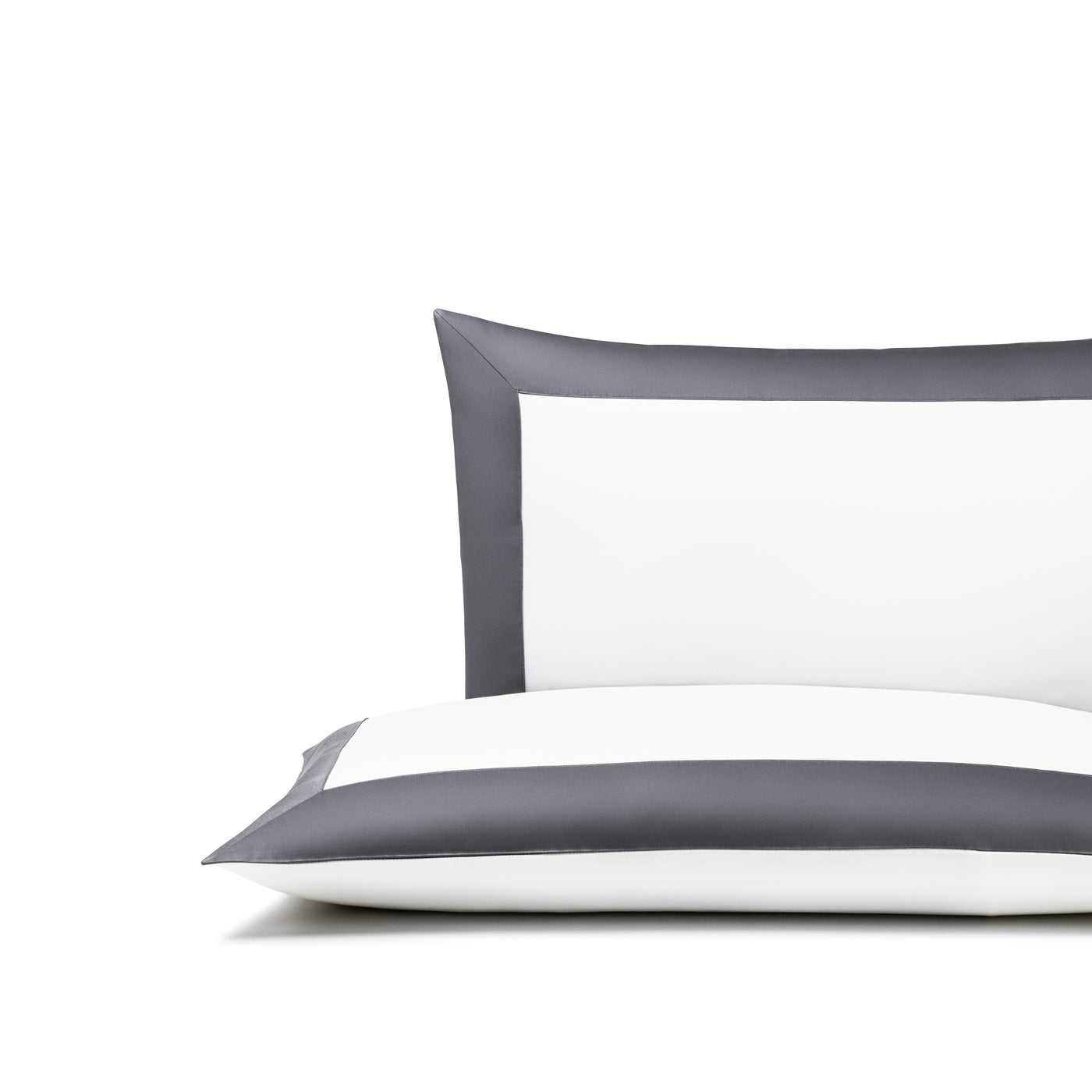 The Bold | Sleeping Sham by Frette, a white pillow with dark gray edges made from soft cotton sateen, is shown in front of a matching pillow against a white background.