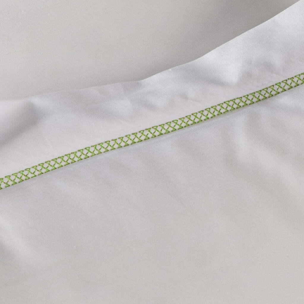 Close-up of lime green geometric embroidered trim on white cotton pillowcase.