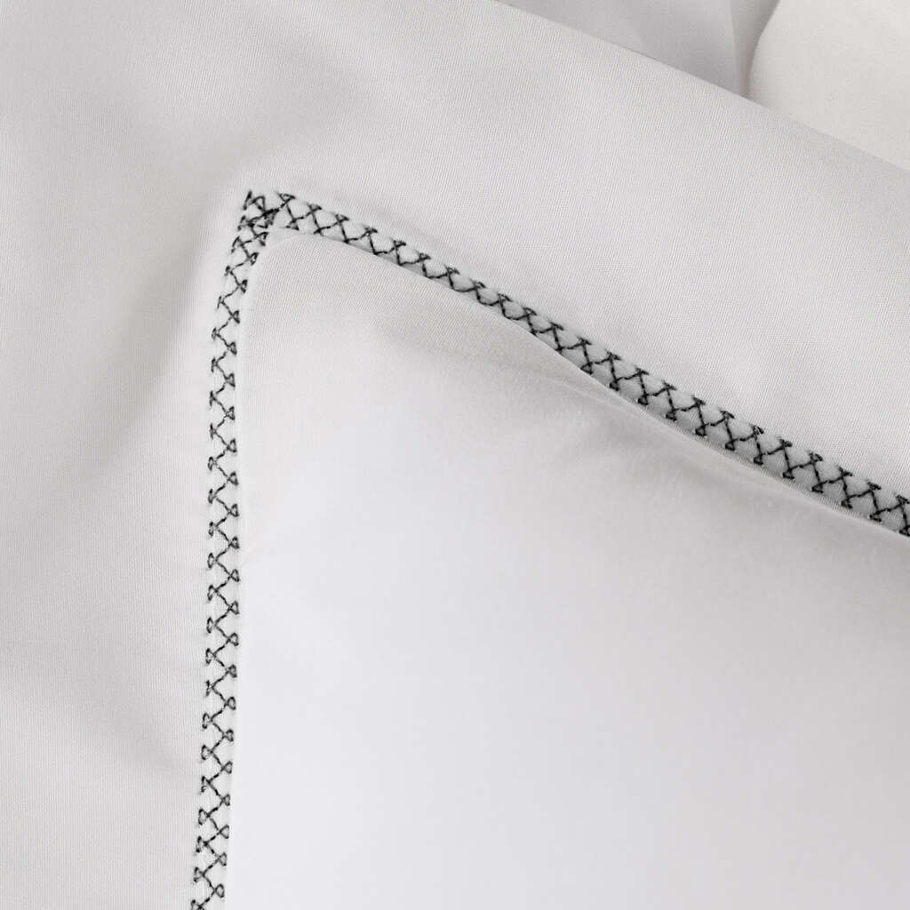 Close-up of black cross-stitch embroidered border on white cotton pillowcase edge.