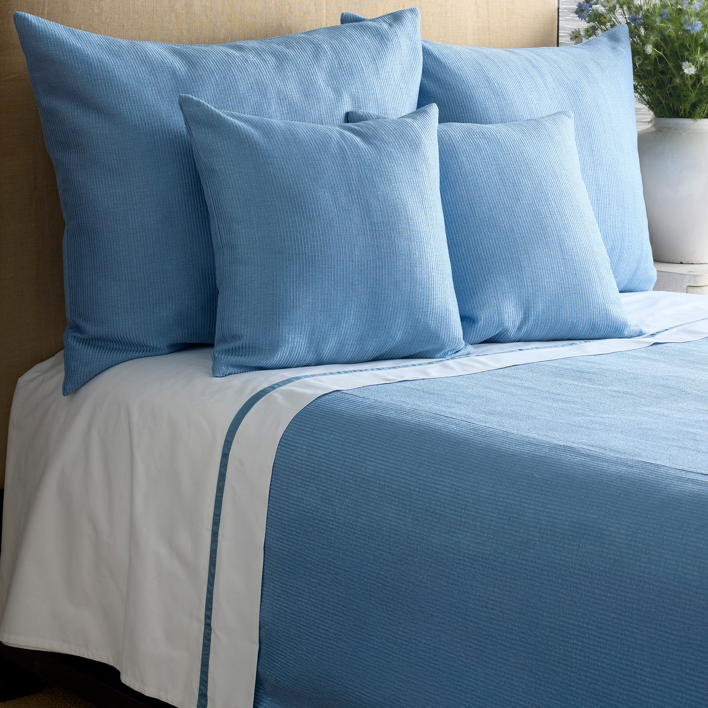 Cornflower blue textured coverlet with white sheet border detail, styled with matching pillows.