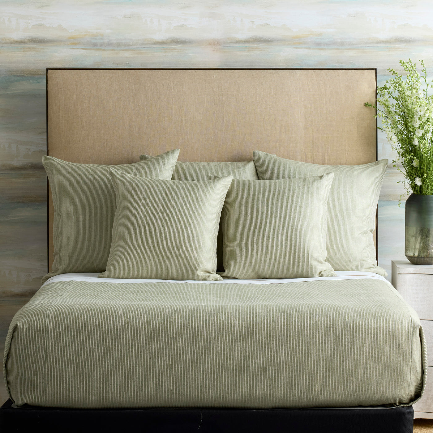 Sage green textured coverlet and pillows styled on a made bed, linen headboard backdrop.