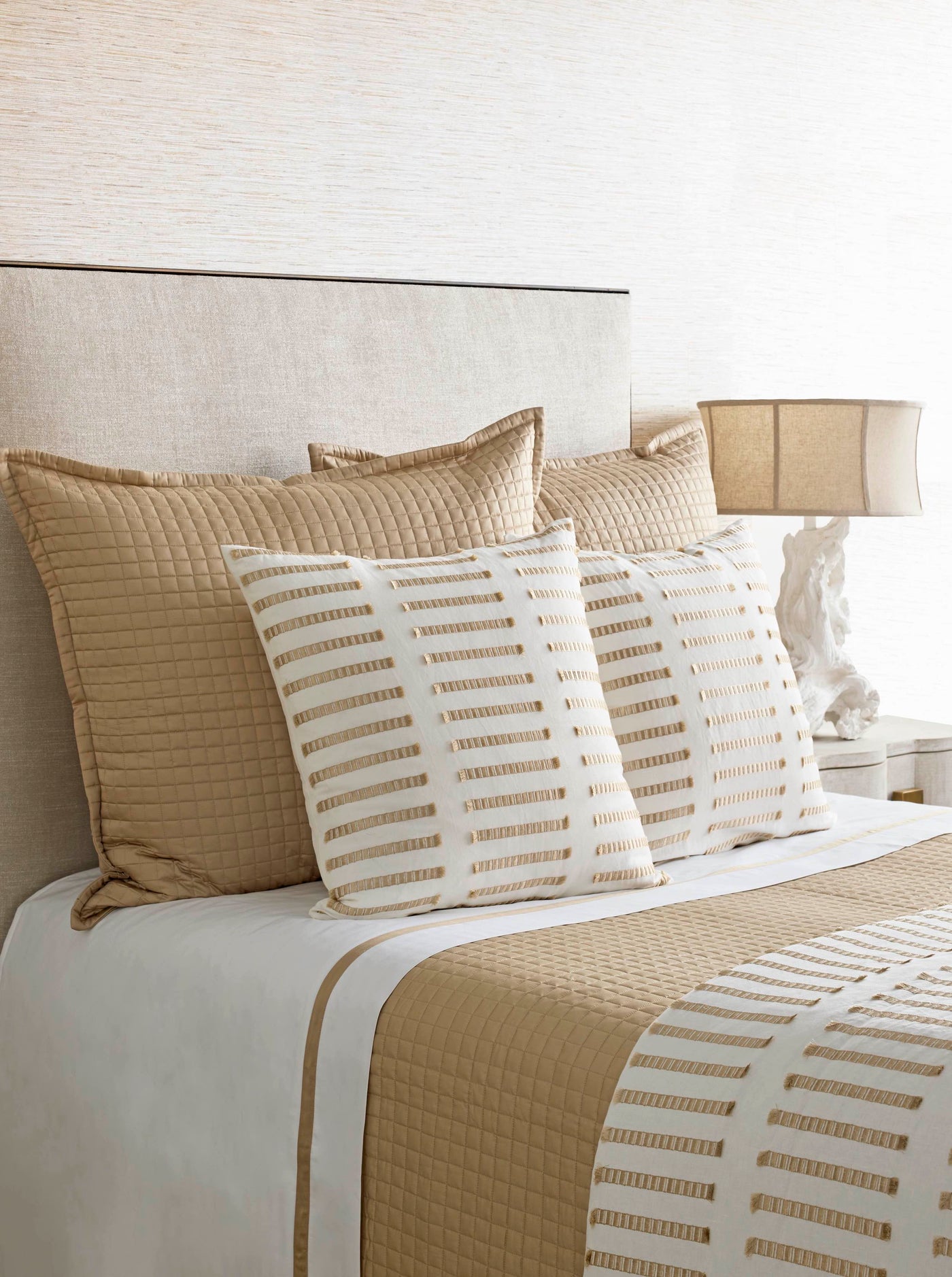 Close-up of ivory pillow with champagne dash stripe pattern against quilted gold bedding.