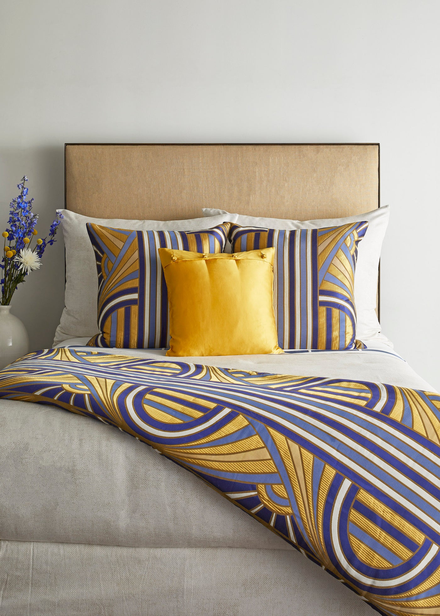 Styled bed scene with blue and gold geometric duvet and matching Ann Gish Lever Du Soleil pillows.