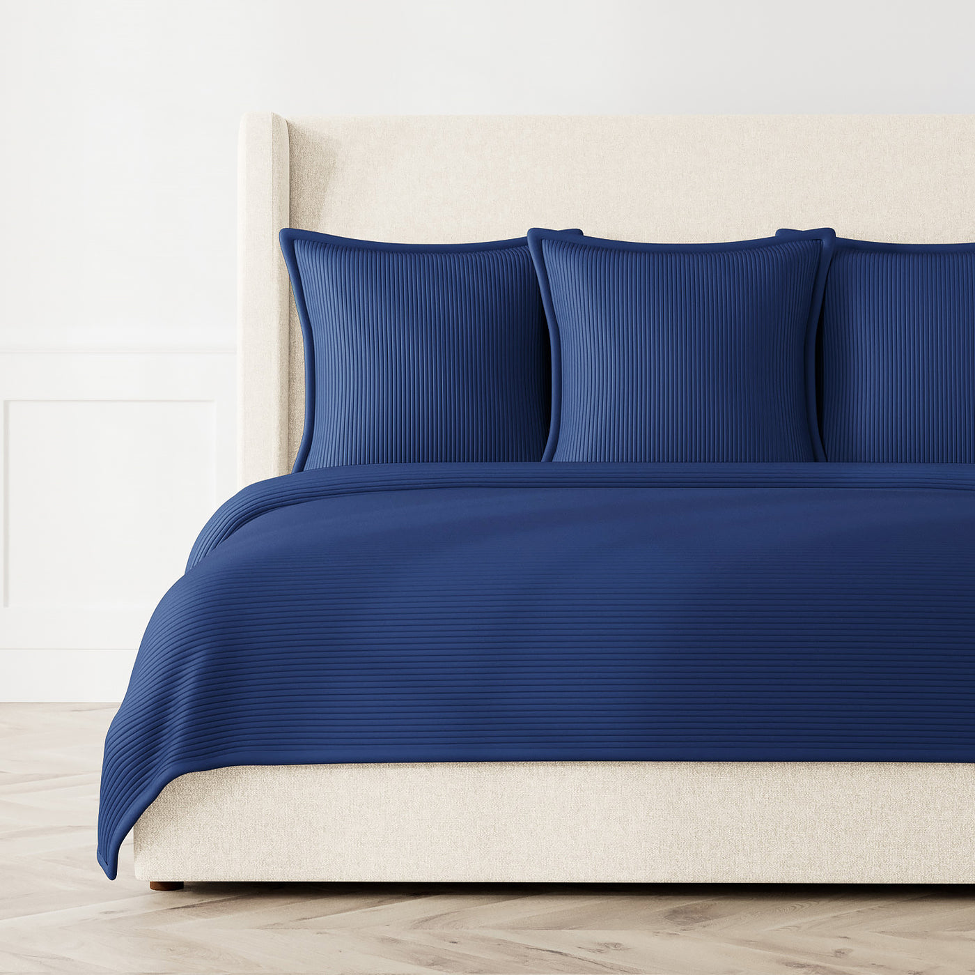 Navy blue textured coverlet and matching shams styled on a bed with cream upholstered headboard.