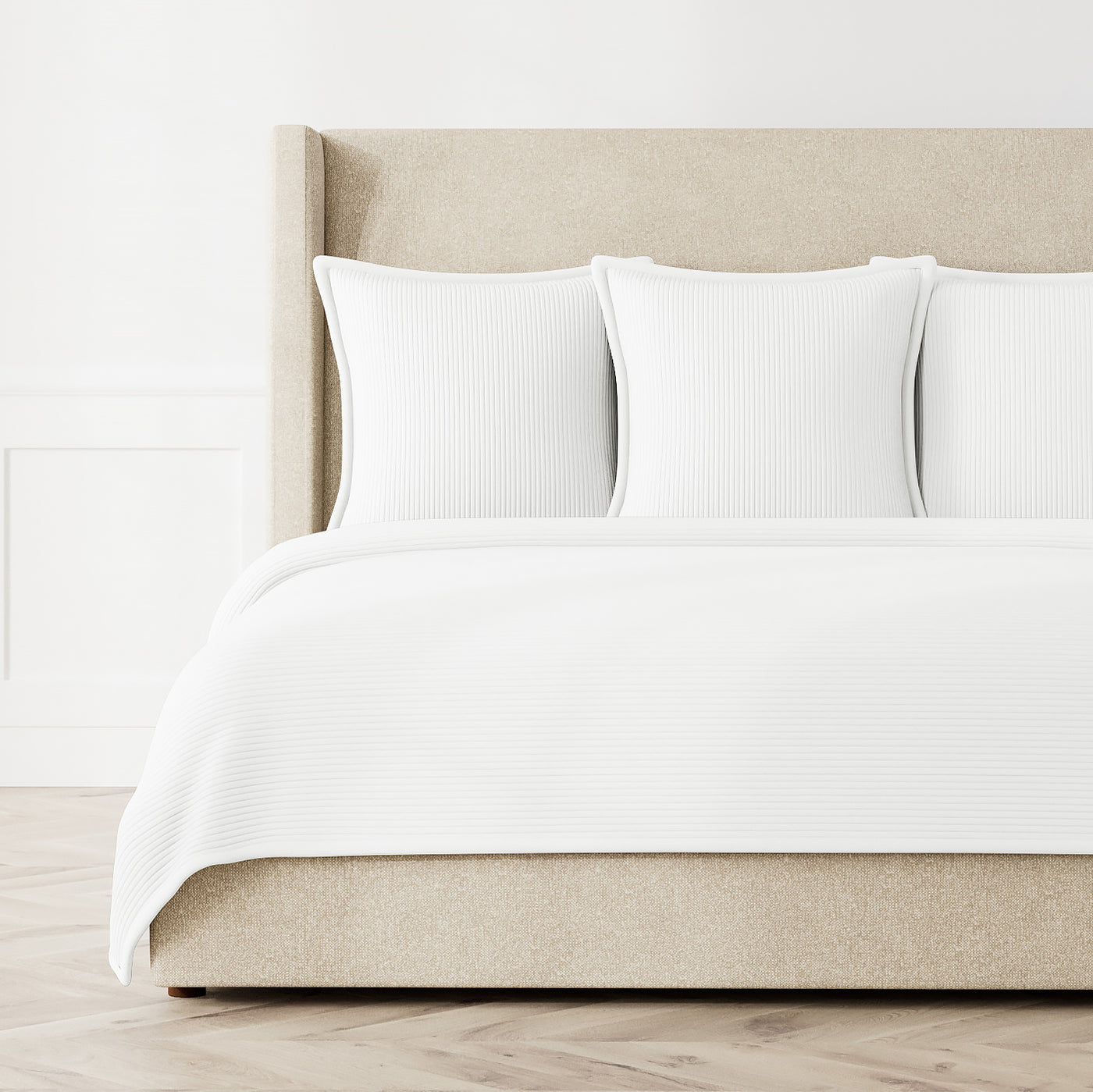 Ribbed white coverlet and matching shams styled on a neutral upholstered bed.