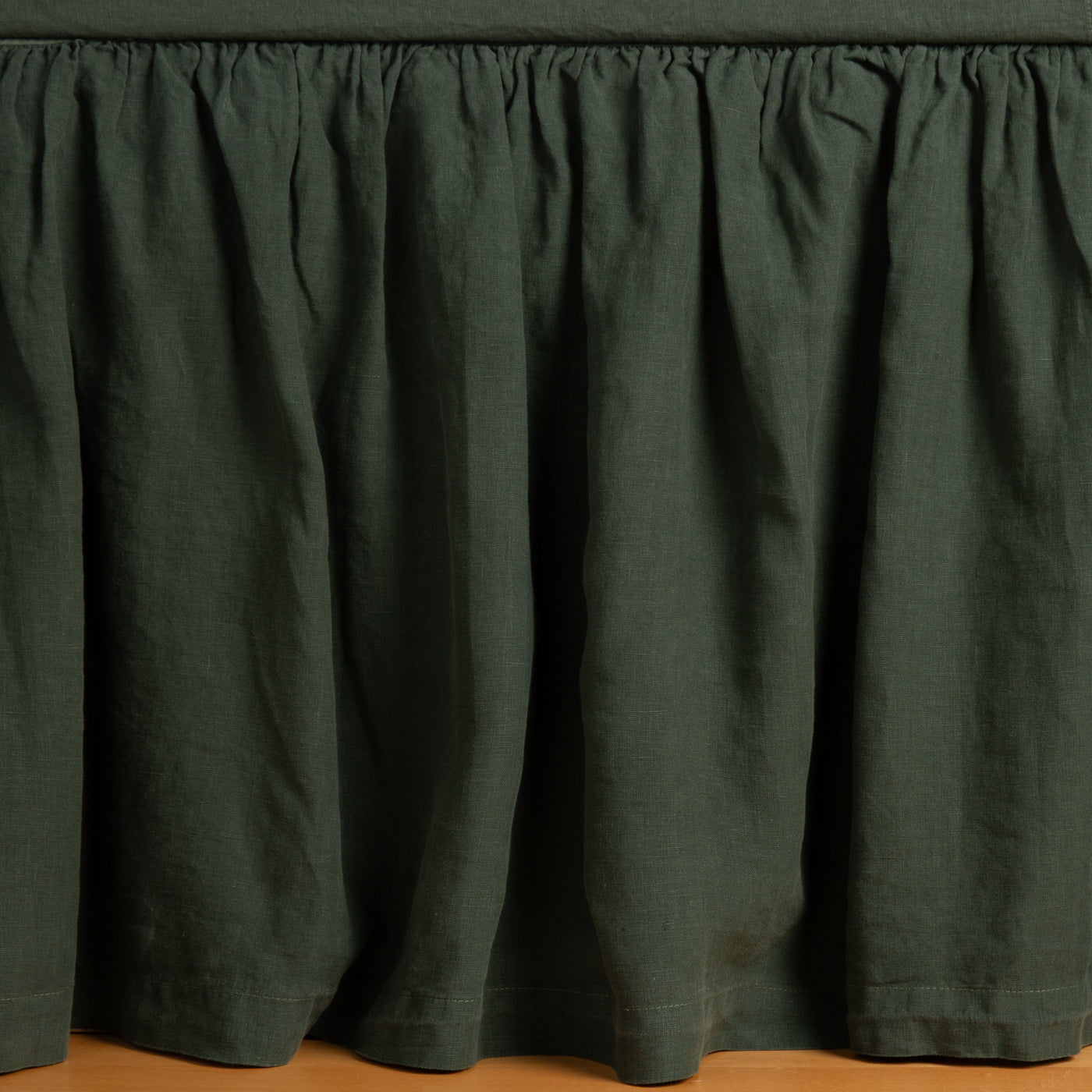 Gathered Juniper linen bed skirt with pleated drop, styled on a bed frame.