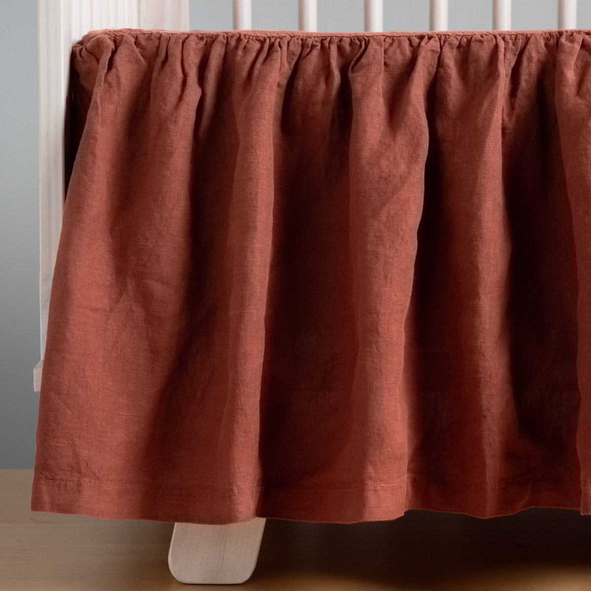 Gathered Autumn linen crib skirt draped along crib base, close view showing texture.