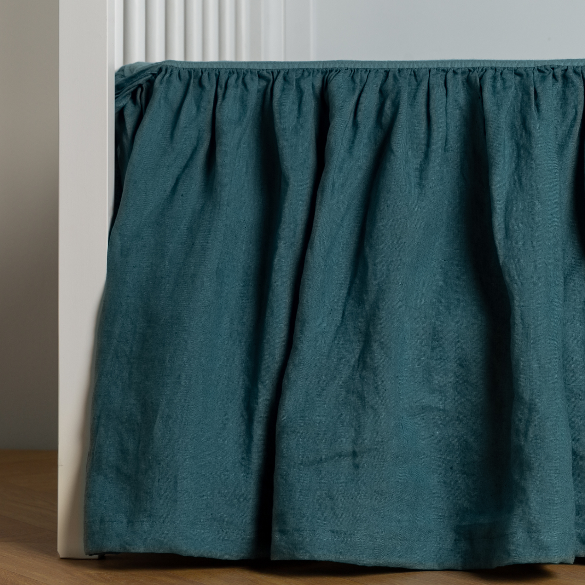 Gathered Cenote linen crib skirt draped to the floor, close view of ruffled skirt panel.