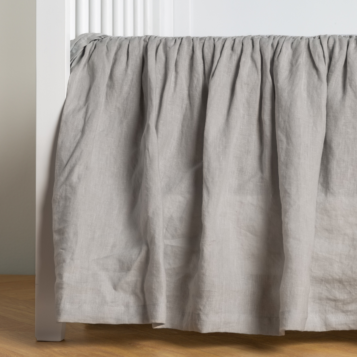 Bella Notte Linen crib skirt in Cloud, showing gathered ruffle drape on a white crib.