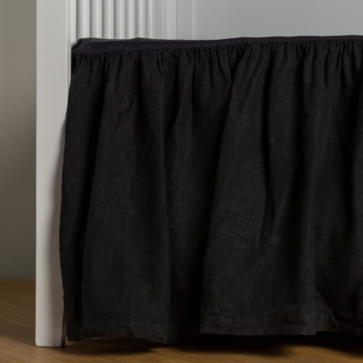 Bella Notte Linen crib skirt in Corvino, gathered ruffle draping to floor against white crib frame.