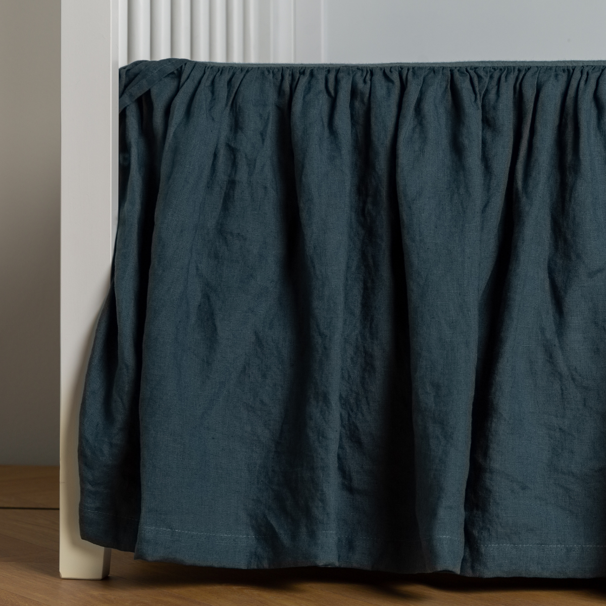 Midnight linen crib skirt with gathered ruffle draping to wood floor.