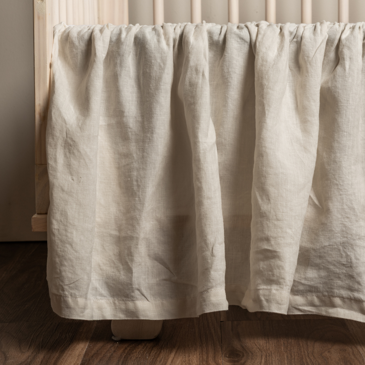 Natural linen crib skirt draped over a crib rail, showing gathered fabric and relaxed texture.