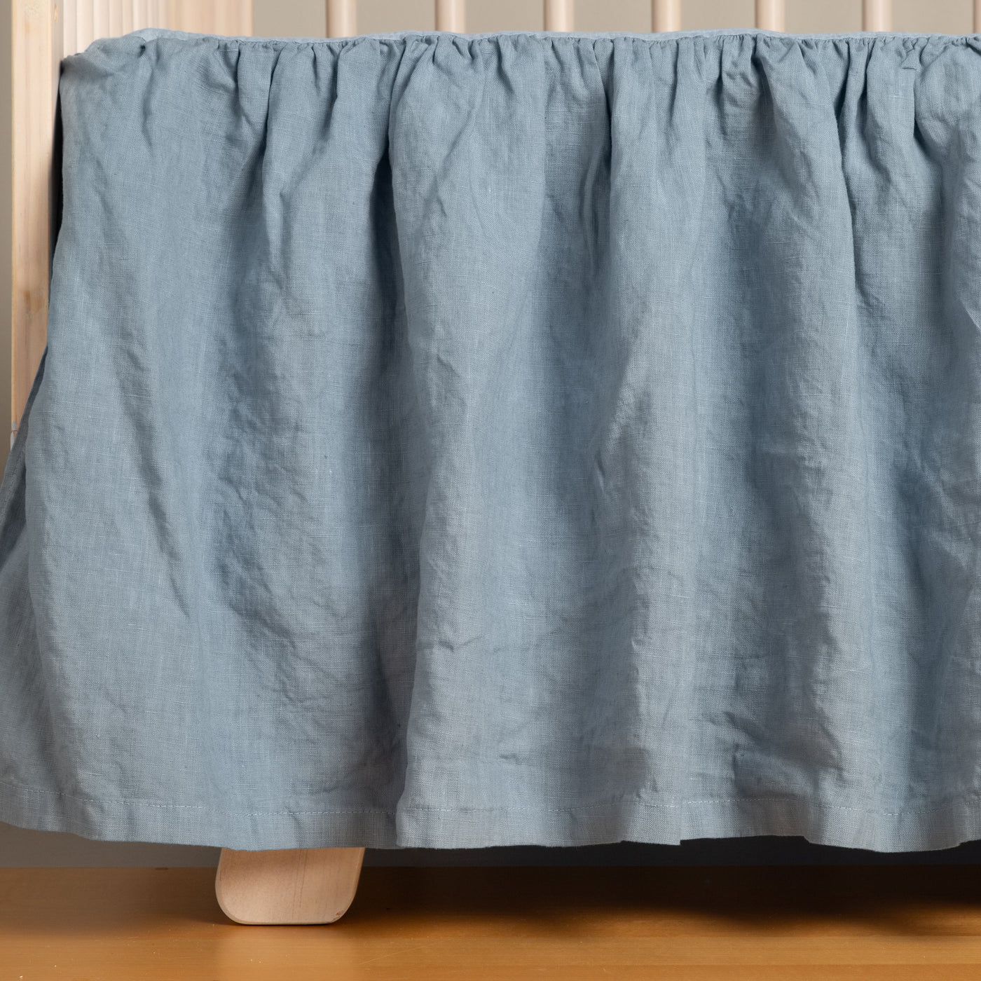 Gathered Tahoe Blue linen crib skirt draped to the floor, showing natural washed texture.