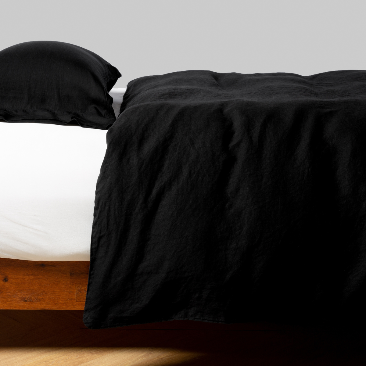 Bella Notte Linen duvet cover in Corvino draped over bed with matching pillowcase, angled side view.