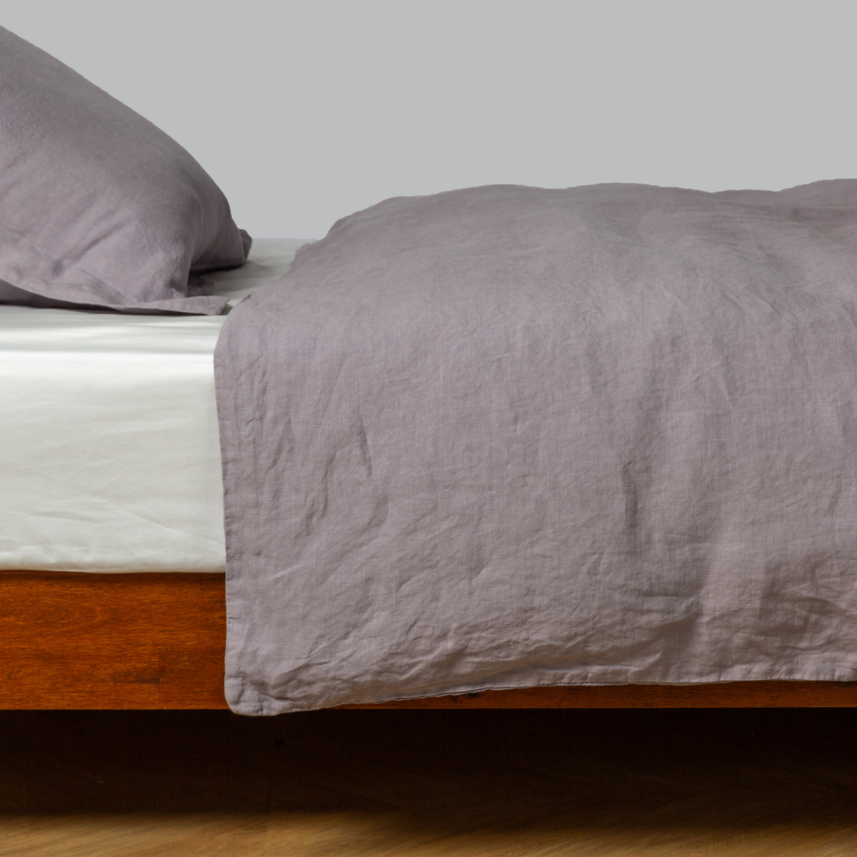 Relaxed washed linen duvet cover in French Lavender styled on a low wood-frame bed.