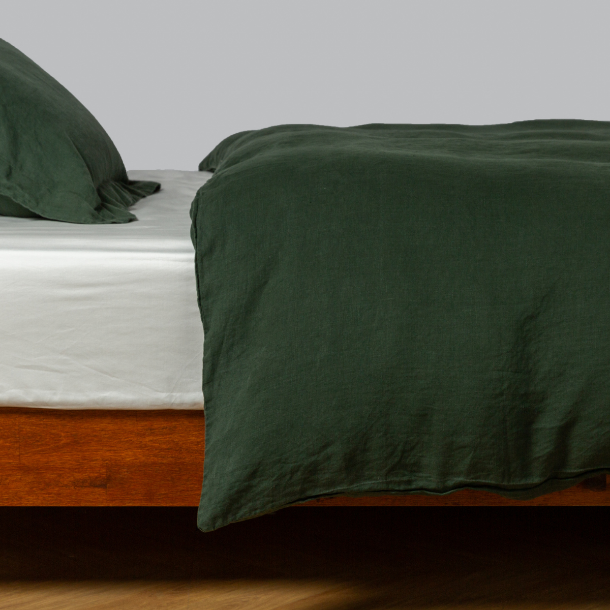 Angled view of Bella Notte linen duvet cover in Juniper draped over a wood platform bed.