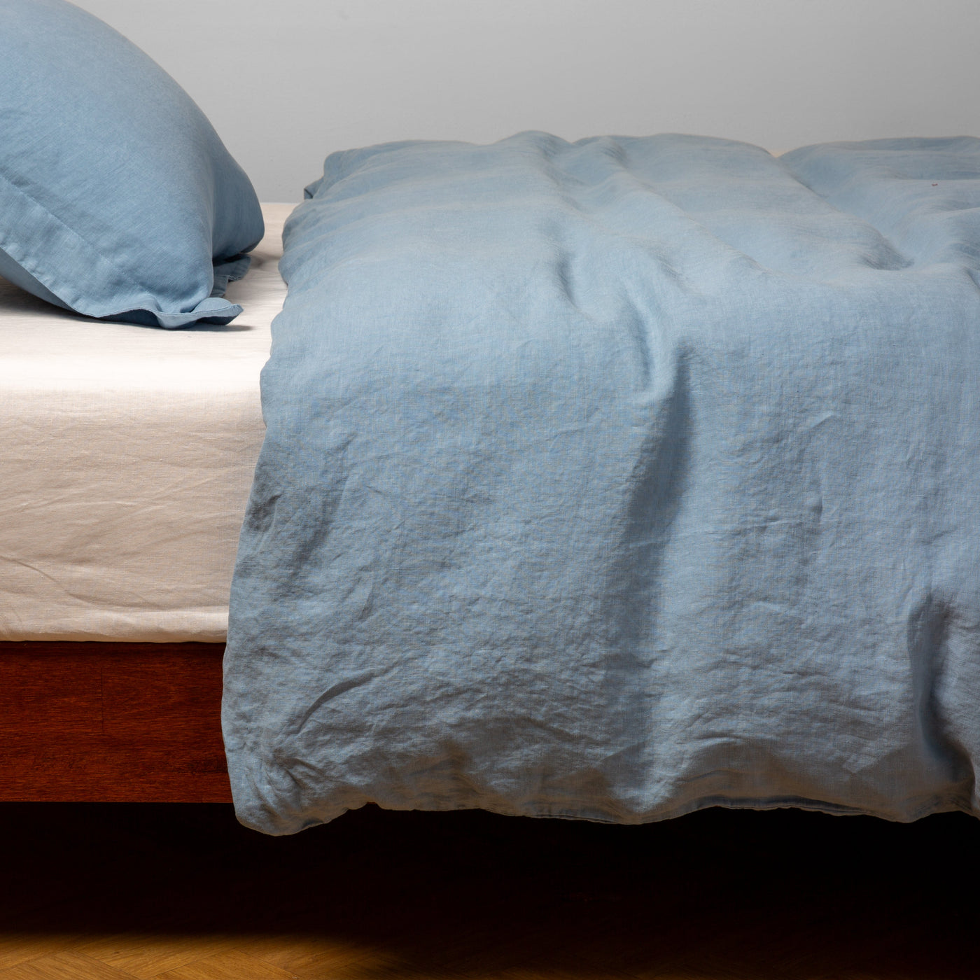 Bella Notte Linen duvet cover in Tahoe Blue, draped over bed with matching pillow sham.