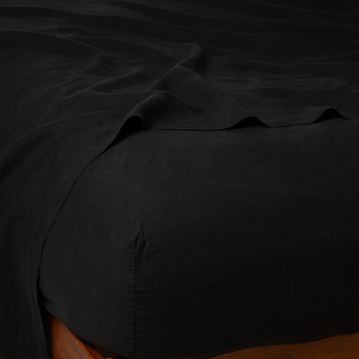Corvino linen fitted sheet corner detail on wooden bed frame, with draped flat sheet.