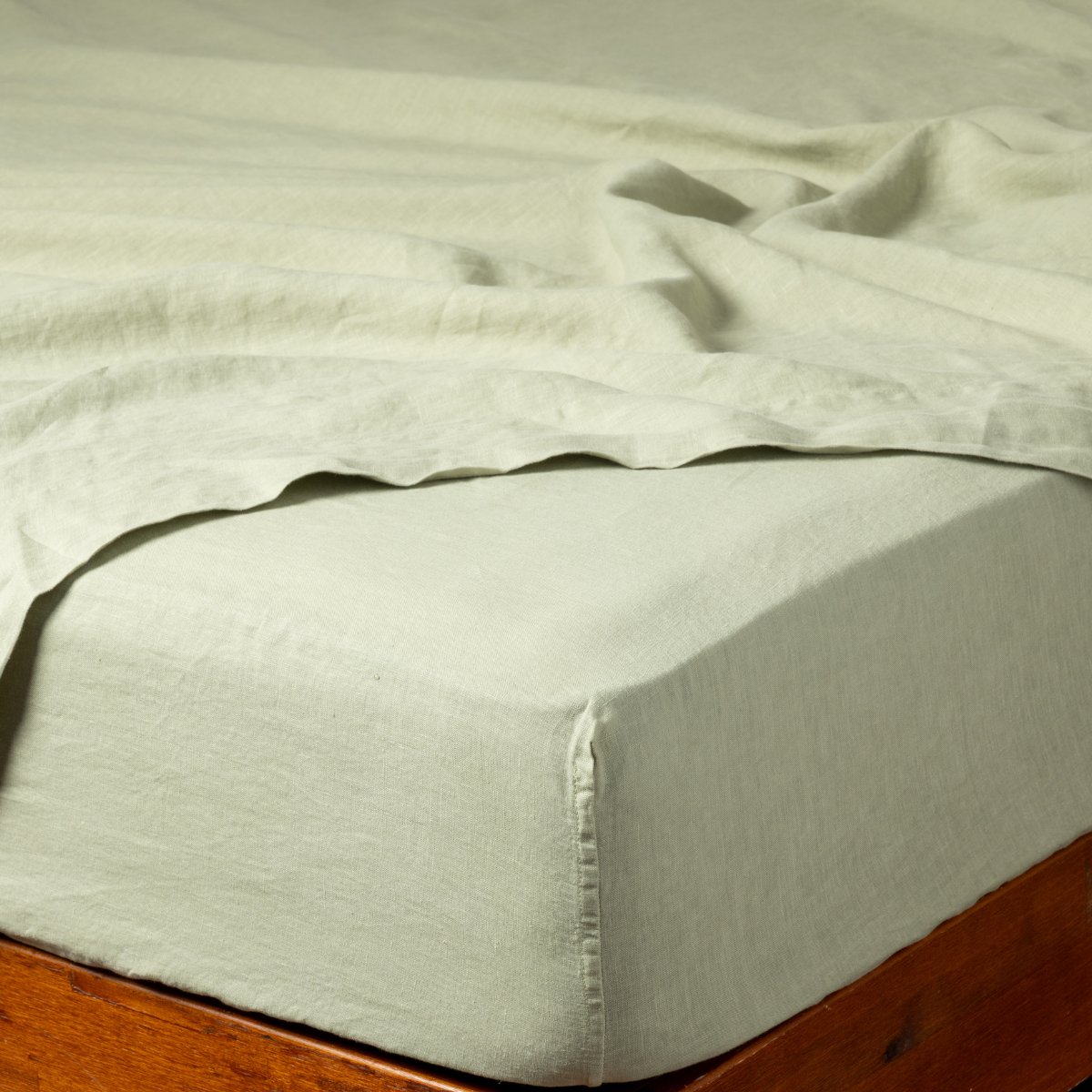 Close-up of Bella Notte Desert Sage linen fitted sheet tucked on wood bed frame.