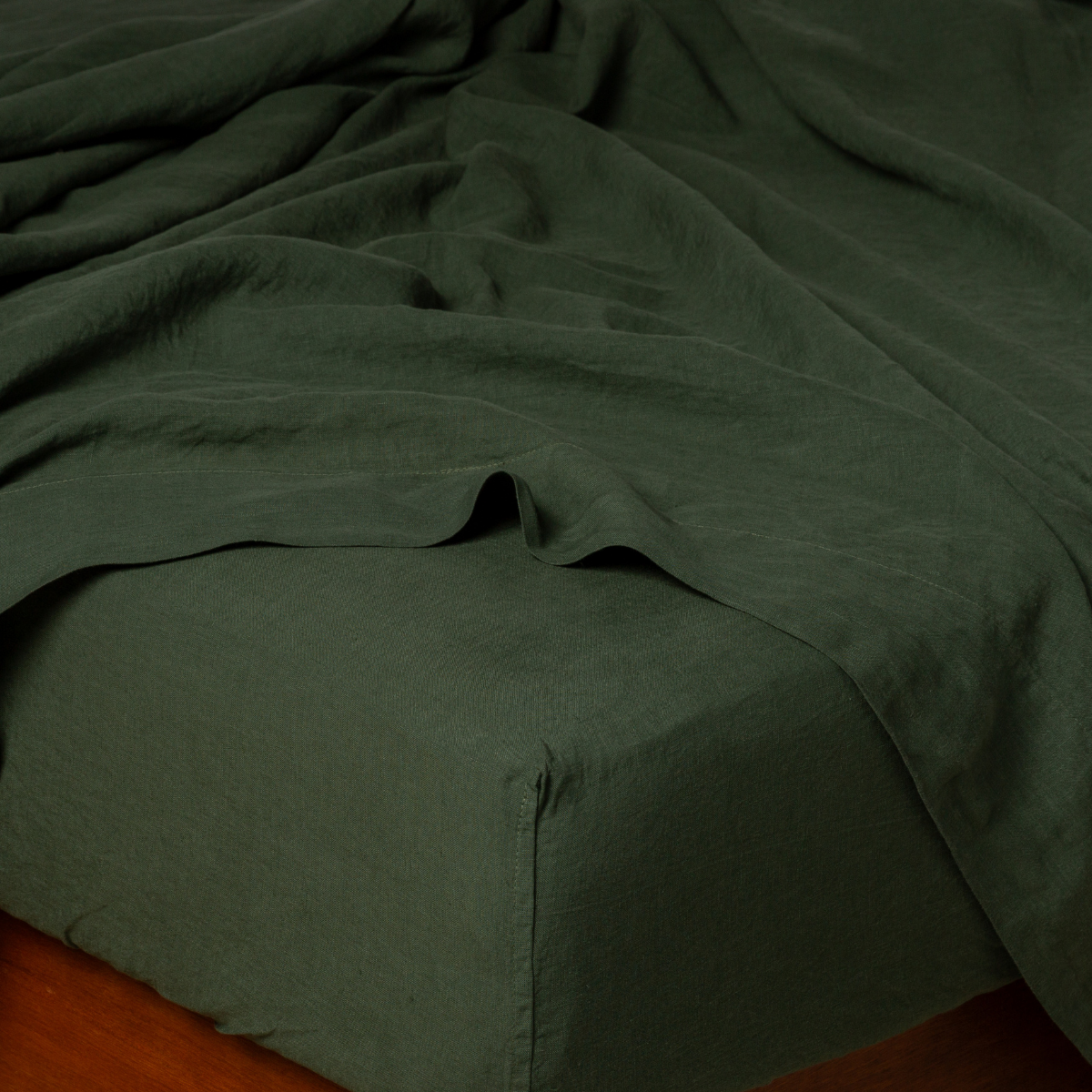 Bella Notte Linen fitted sheet in Juniper, casually draped flat sheet detail on corner.