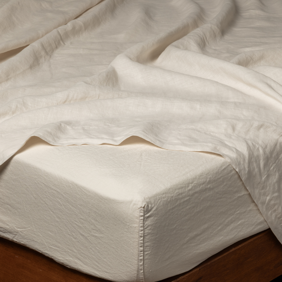 Bella Notte Linen fitted sheet in Natural, corner detail on bed with softly rumpled flat sheet.