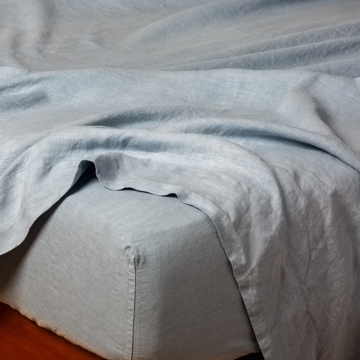 Bella Notte Linen fitted sheet in Tahoe Blue, draped loosely over bed corner showing relaxed texture.