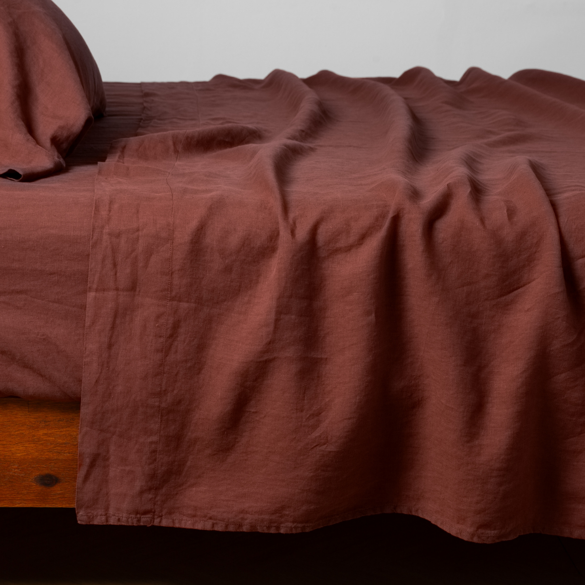 Bella Notte Linen flat sheet in Autumn, draped loosely over a wooden bed frame.