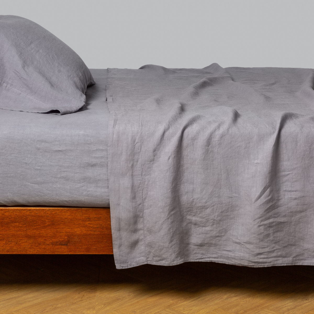 Bella Notte Linen flat sheet in French Lavender draped casually over a wood-frame bed.