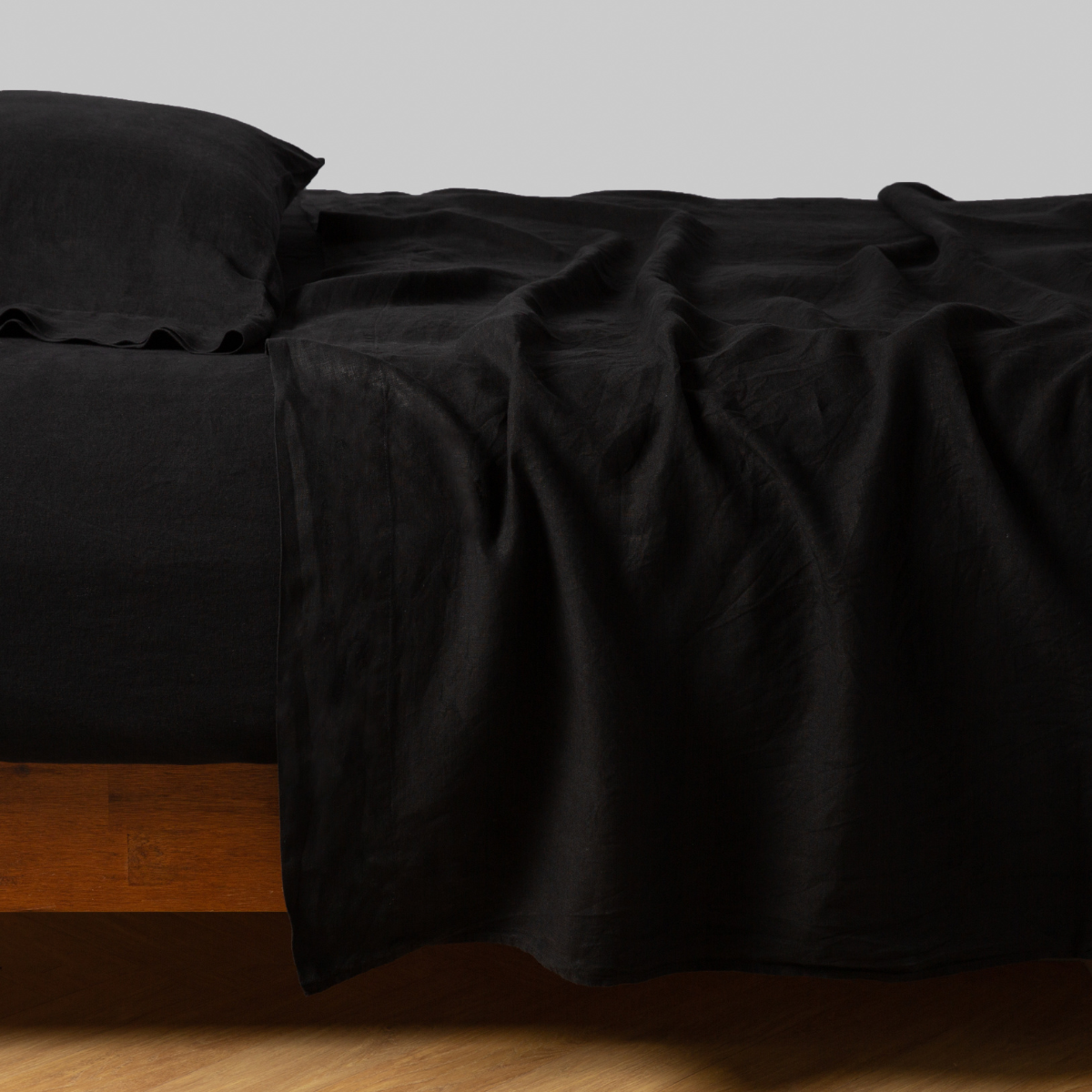 Corvino flat sheet draped loosely over a wood-frame bed with matching pillowcase.