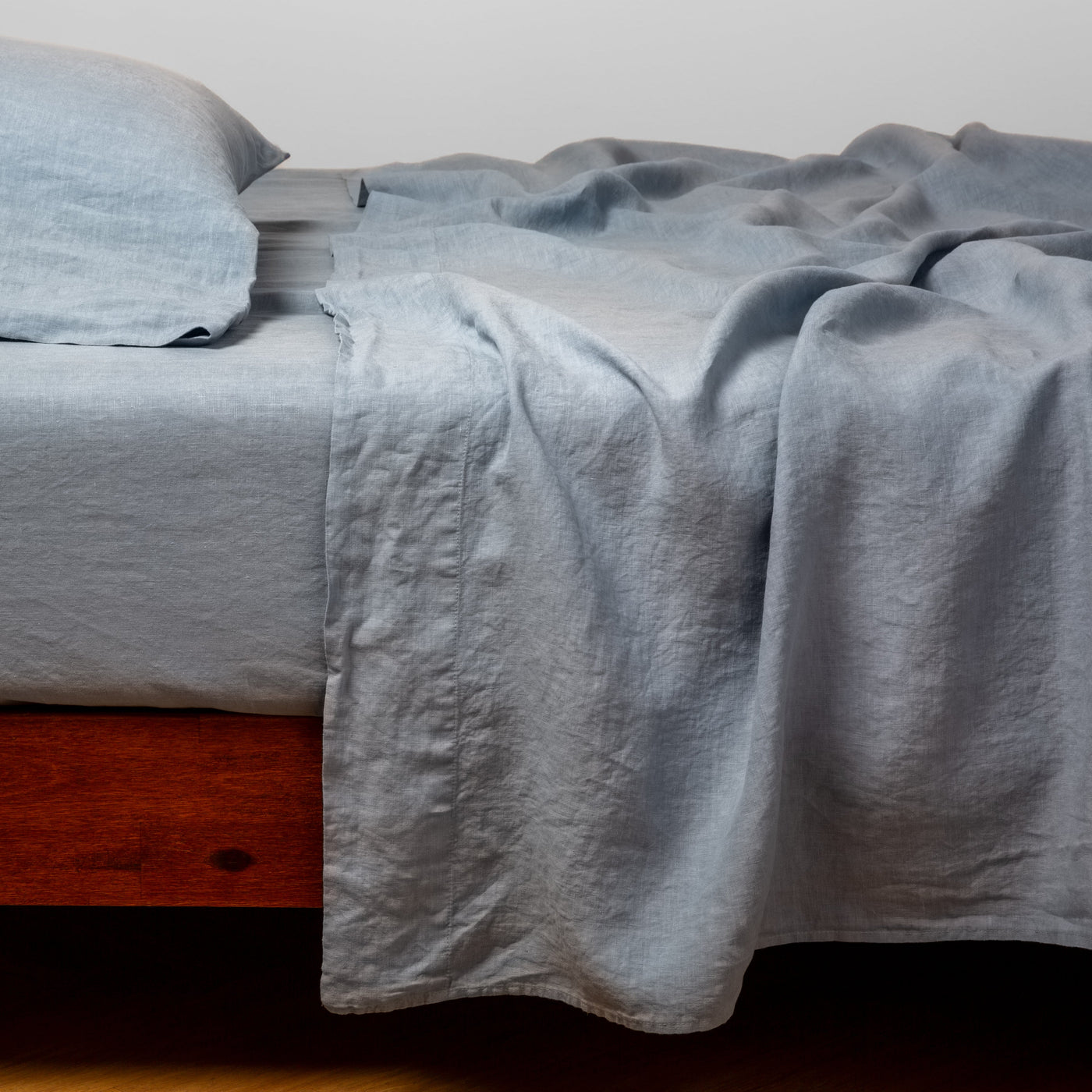Bella Notte Linen flat sheet in Tahoe Blue, draped loosely over a wood-frame bed.