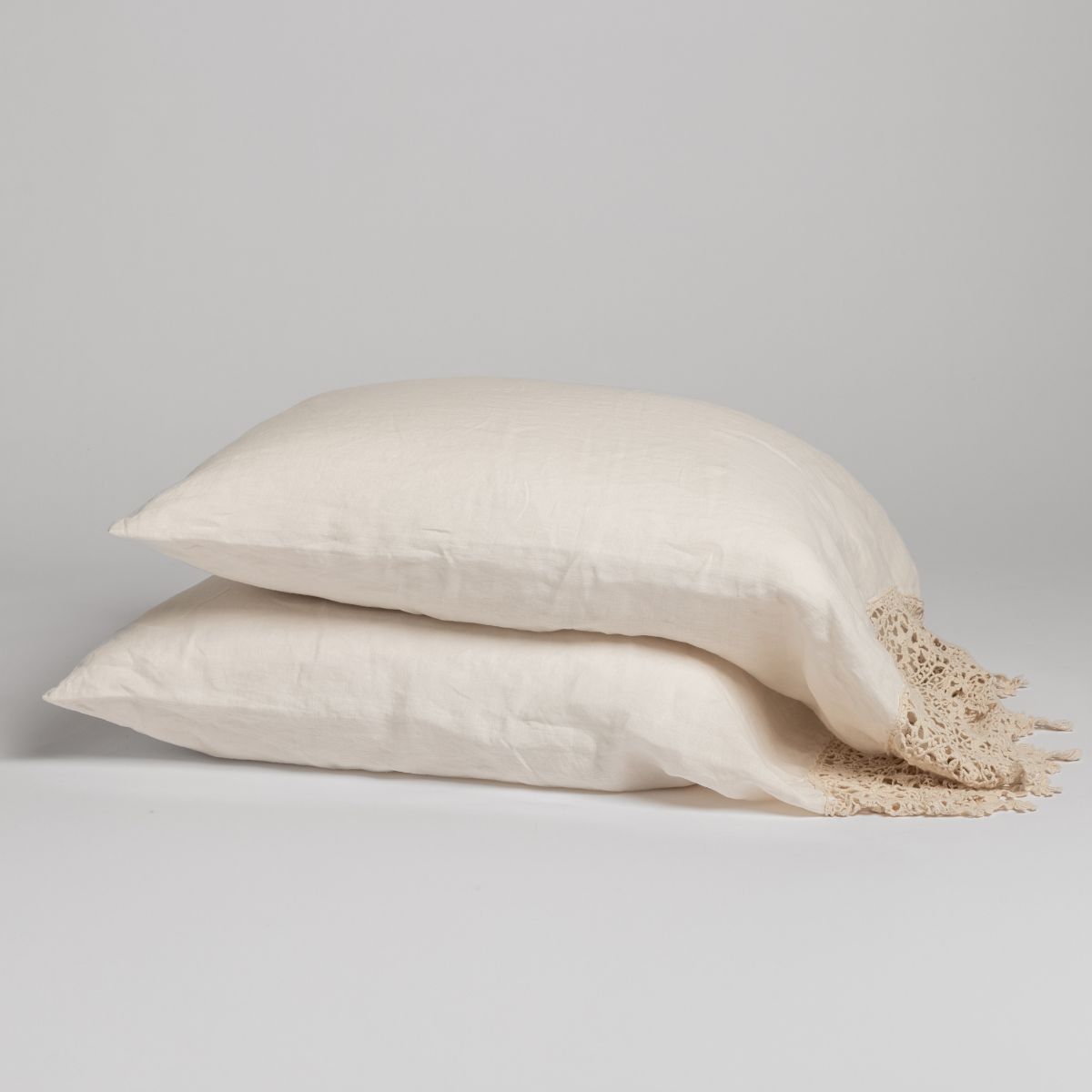Two stacked Natural linen pillowcases with crochet lace trim, shown against a grey background.