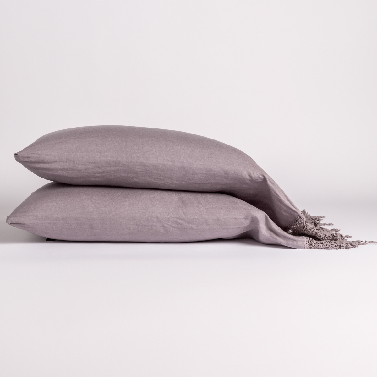 Two French Lavender linen pillowcases stacked, with knotted fringe trim visible at right edge.