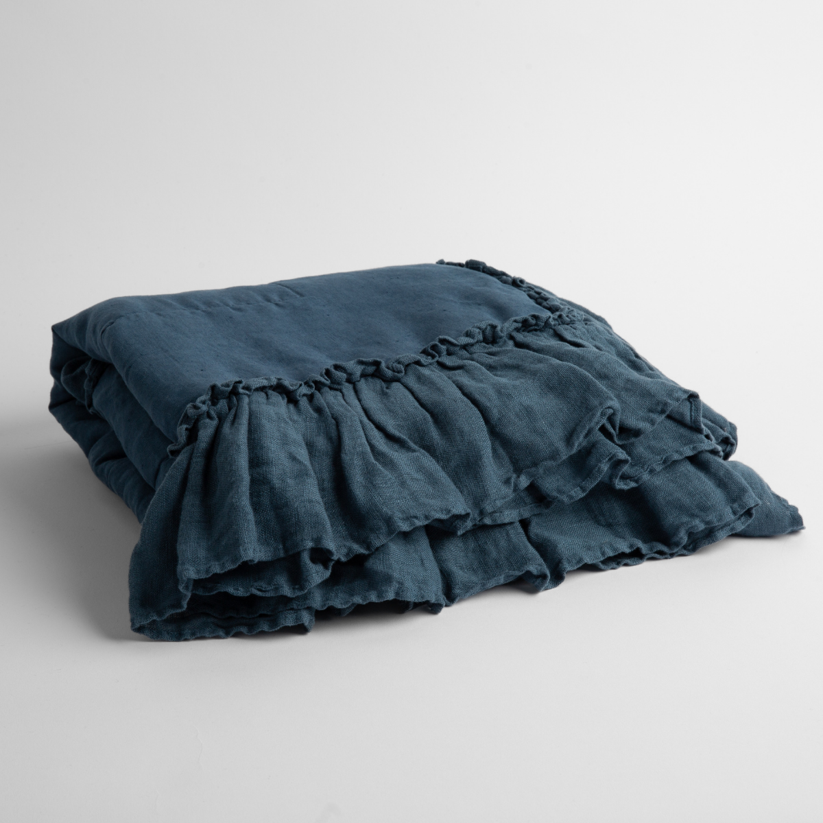 Folded Midnight linen baby blanket showing double ruffle trim detail along front edge.